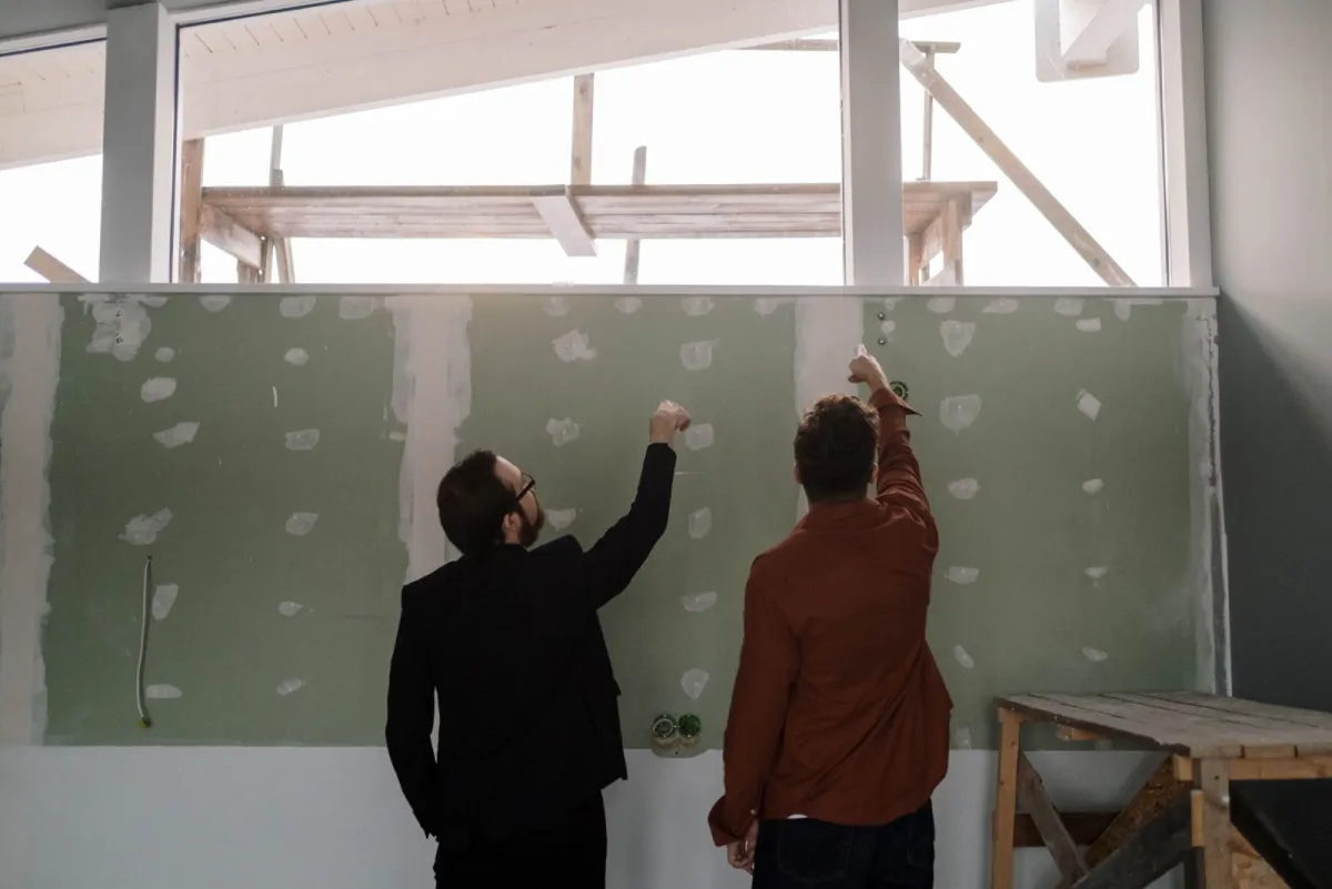 Two people looking over a hung and spotted drywall wall before finishing starts
